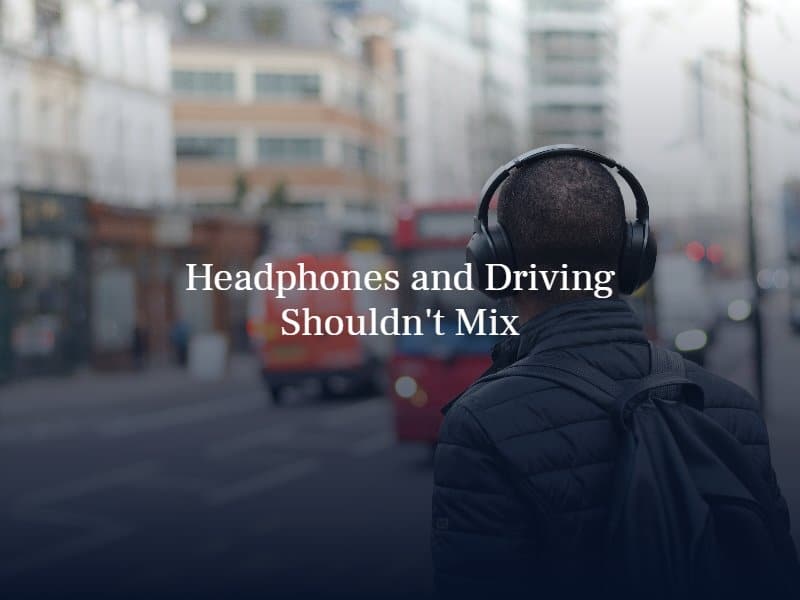 man wearing headphones standing on the sidewalk | text: headphones and driving shouldn't mix