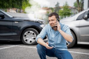 A man on the phone in front of a car accident, asking how long a car accident settlement takes.